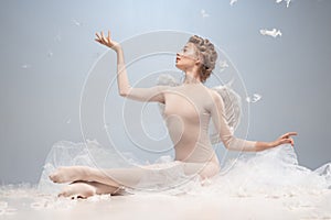 Portrait of pretty, slim beautiful young girl, graceful ballerina in image of angel with wings sitting on cloud isolated