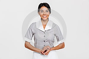 Portrait of pretty smiling maid in uniform keeping hands together and looking at camera