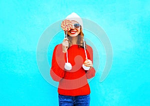 Portrait pretty smiling woman closes face with lollipop in red knitted sweater