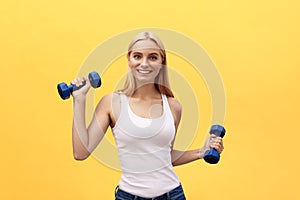 Portrait of pretty sporty girl holding weights and smiling. Isolated over yellow background.