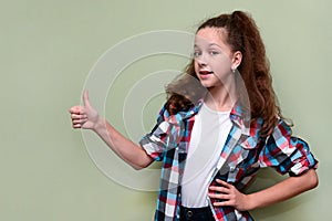 portrait of pretty teenage girl in white T-shirt and plaid shirt shows raised thumb, expressing her consent.