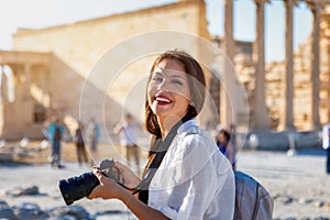 Portrait of a pretty tourist woman with a photo camera in her hand in front of the Acropolis of Athens, Greece