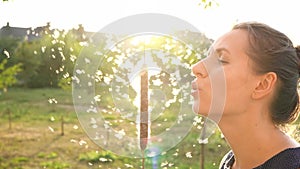 Portrait of pretty woman blows on reeds outdoors in sunny day. Fluff from reeds flies around