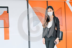 Portrait of pretty woman with mask stand in front of door of sky train on the platform during coronavirus pandemic in city