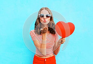 Portrait pretty woman sends air kiss with red balloon heart shape over blue