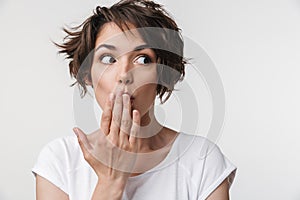 Portrait of pretty woman with short brown hair in basic t-shirt covering her mouth with hand