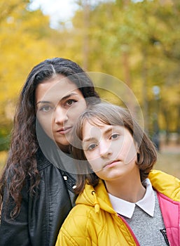 Portrait of pretty woman and teen girl. They are posing in autumn park. Beautiful landscape at fall season