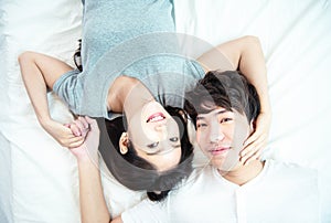 Portrait of pretty young asian couple with happiness. asia man and woman lay on bed facing together with big smile hand cover face