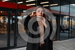 Portrait of a pretty young brunette woman with natural make-up with beautiful sexy lips in a black vintage coat in a beige trendy