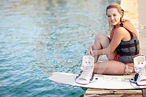 Portrait of a pretty young girl sitting on a jetty next to a wakeboard. Portrait of a pretty young girl sitting on a