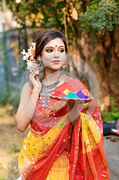 Portrait of pretty young indian girl wearing traditional saree and jewellery, holding powder colours in plate