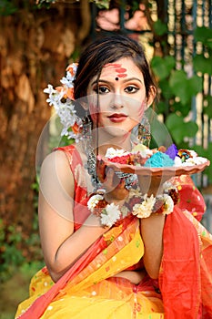 Portrait of pretty young indian girl wearing traditional saree and jewellery, holding powder colours in plate on the festival of