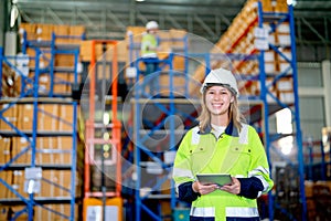 Portrait of pretty young warehouse worker woman hold tablet and look at camera with smiling and her co-worker work on the