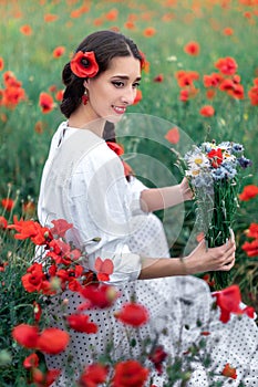 Portrait of a pretty young woman on the background of a blooming poppy field. Ukrainian woman sitting with a bouquet of