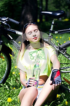 Portrait of pretty young woman with bicycle in a park - outdoor. girl sitting on the grass and drinks water from a