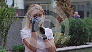 Portrait of pretty young woman in black gloves looking into the camera and putting on medical mask on face for