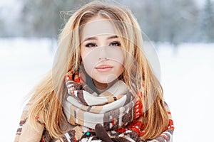 Portrait of a pretty young woman with brown eyes with beautiful makeup with long blond hair in a woolen vintage warm scarf