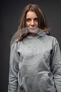 Portrait of pretty young woman with brunette hair in oversize gray hoodie, stands on dark background. lifestyle fashion concept