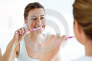 Pretty young woman brushing her teeth in the bathroom at home. photo
