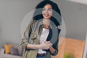 Portrait of pretty young woman contemplate hold pen clipboard wear khaki shirt modern interior house indoors