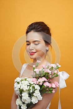 Portrait of a pretty young woman holding bouquet of carnation  over yellow background