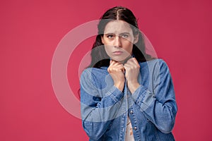 Portrait of a pretty young woman in a light dress and blue shirt standing on pink background in studio. People sincere