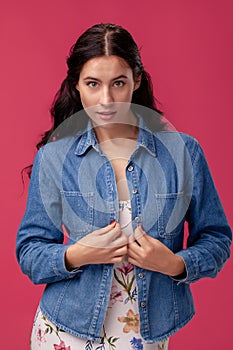 Portrait of a pretty young woman in a light dress and blue shirt standing on pink background in studio. People sincere