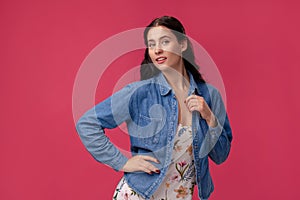 Portrait of a pretty young woman in a light dress and blue shirt standing on pink background in studio. People sincere