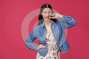 Portrait of a pretty young woman in a light dress and blue shirt standing on pink background in studio. People sincere