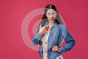 Portrait of a pretty young woman in a light dress and blue shirt standing on pink background in studio. People sincere