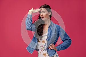 Portrait of a pretty young woman in a light dress and blue shirt standing on pink background in studio. People sincere