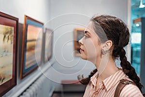 Portrait of a pretty young woman looking at a painting. An exhibition in an art gallery. Excursion and visit to the