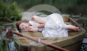 Portrait of pretty young woman lying in the boat on river bank.