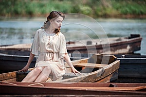 Portrait of pretty young woman sitting in the boat on river bank.