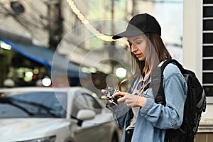 Portrait of pretty young woman traveler wearing hat and backpack standing on busy city street in the evening