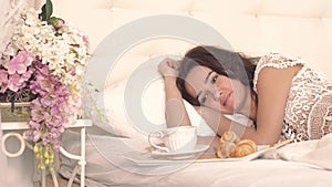 Portrait of pretty young woman waking up because of her husband bringing her breakfast in bed