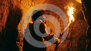 Portrait of Primeval Caveman Wearing Animal Skin Exploring Cave At Night, Holding Torch with Fire