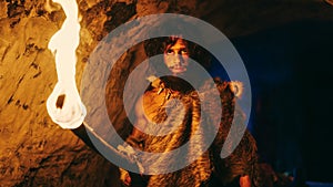 Portrait of Primeval Caveman Wearing Animal Skin Exploring Cave At Night, Holding Torch with Fire