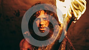 Portrait of Primeval Caveman Wearing Animal Skin Standing in His Cave At Night, Holding Torch with