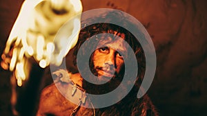 Portrait of Primeval Caveman Wearing Animal Skin Standing in His Cave At Night, Holding Torch with