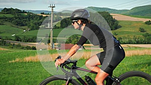 Portrait of pro female cyclist on bicycle. Fit muscular woman athlete riding bike uphill at sunset. Confident concentrated road cy