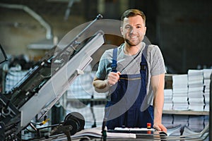 Portrait of production line worker controlling manufacturing process of modern packaging industrial machine in printing