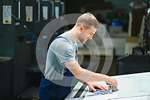 Portrait of production line worker controlling manufacturing process of modern packaging industrial machine in printing