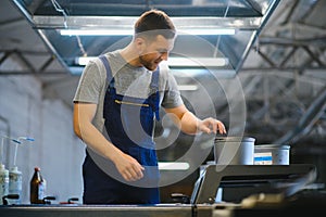 Portrait of production line worker controlling manufacturing process of modern packaging industrial machine in printing