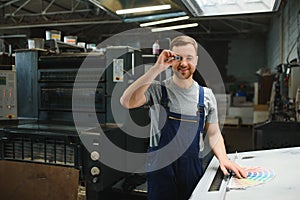 Portrait of production line worker controlling manufacturing process of modern packaging industrial machine in printing