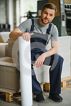 Portrait of production line worker controlling manufacturing process of modern packaging industrial machine in printing