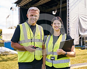 Portrait Of Production Team With Headsets Setting Up Outdoor Stage For Music Festival Or Concert