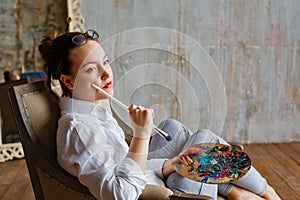 Portrait of a professional artist. A female artist draws. A girl in glasses, a white shirt and jeans with a brush and palette