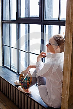 Portrait of a professional artist. A female artist draws. A girl in glasses, a white shirt and jeans with a brush and palette