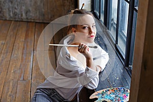 Portrait of a professional artist. A female artist draws. A girl in glasses, a white shirt and jeans with a brush and palette